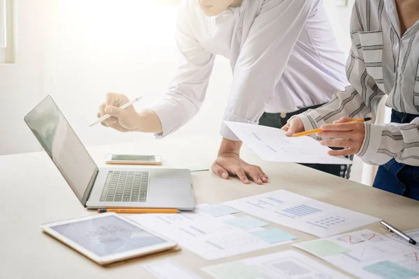 Two brokers standing by desk in front of laptop and discussing online data