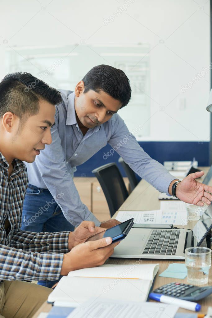 Vietnamese UI designer showing ideas his Indian coworker at meeting