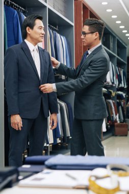 Atölye asistanı olgun müşteri takım elbise seçmek için yardımcı 
