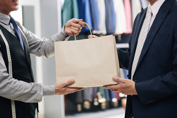 Man receiving paper-bag from menswear shop assistant