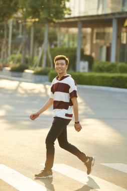 Çekici genç Asyalı adam gülümseyerek ve sokakta yürüyor