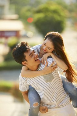 Genç Asyalı adam kız arkadaşını sırtında taşıyor.