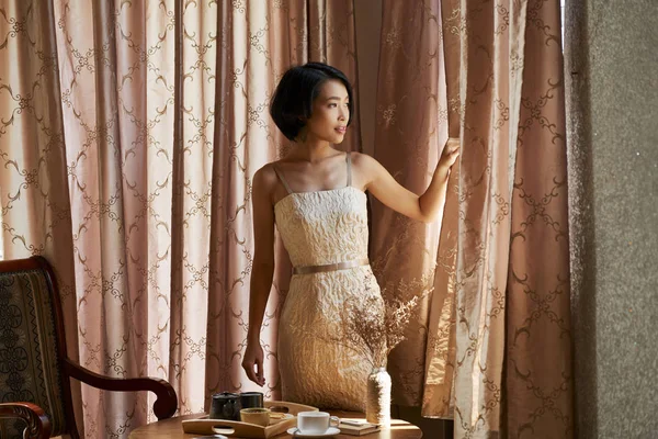 Όμορφη Νεαρή Ασιατική Γυναίκα Άνοιγμα Κουρτίνες Στο Σαλόνι Και Κοιτάζοντας — Φωτογραφία Αρχείου