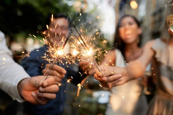 Group of wedding guests burning Bengal lights outdoors at cocktail party