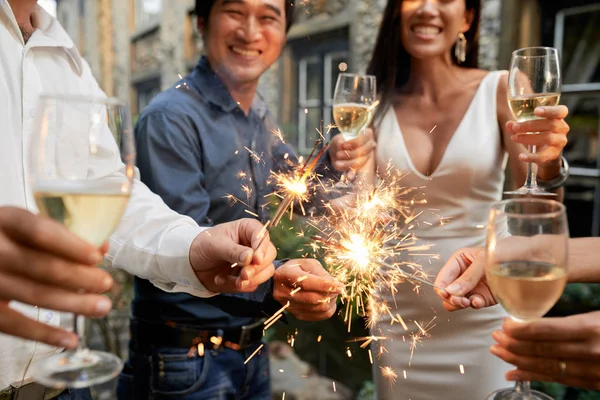 Group of joyful people drinking champagne and burning Bengal lights at great wedding party