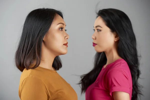 Side view of two serious Asian women standing face to face over grey background
