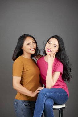 İki genç kız kardeşin gri arka plan üzerinde gülümseyip kameraya poz verme portresi