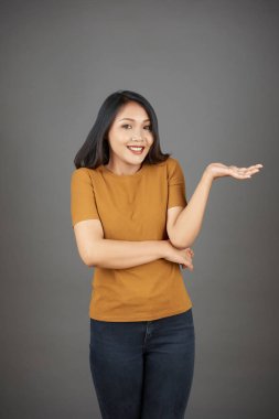 Şaşkın Asyalı genç kadın gri arka plan üzerinde ayakta ne yapacağını bilmiyor