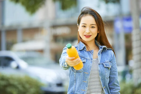 美丽的微笑年轻女子给一瓶橙汁或水果饮料 — 图库照片