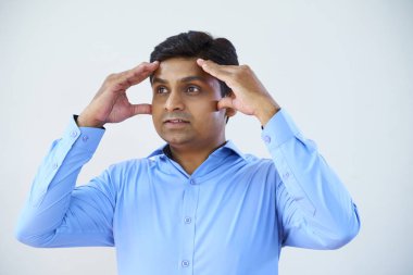 Elleriyle başını tutup beyaz arka planda kalan bir şeyi düşünen genç bir çalışan.