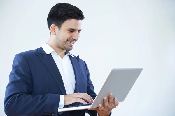 スーツ姿で立つ若いビジネスマンがノートパソコンにタイピングし 白い背景に孤立した笑顔 — ストック写真