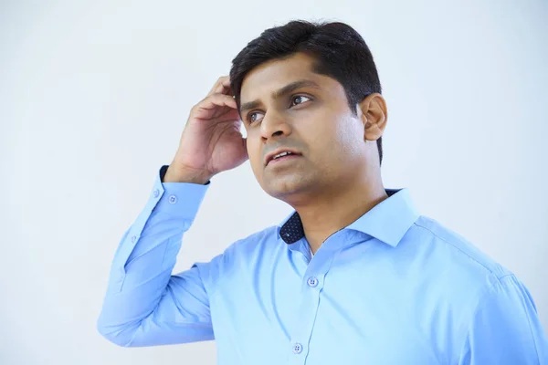 青いシャツを着て頭を掻き 白い背景を見つめるインド人ビジネスマンの肖像画 — ストック写真