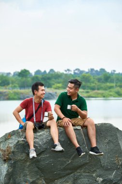 Vietnamlı turistler tırmandıktan sonra büyük kaya üzerinde dinlenirken konuşuyor ve çay içiyor