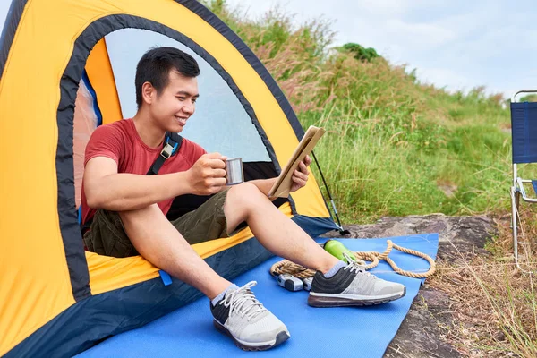 Joyful Asian Man Sitter Tält Dricka Hett Och Läsa Nyheter — Stockfoto