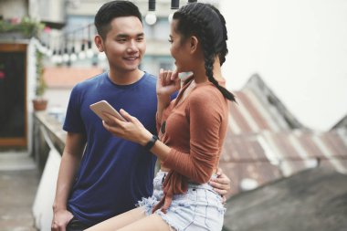 O cep telefonu kullanarak ve açık havada onunla konuşurken Gülümseyen Asyalı adam kız arkadaşı kucaklayan