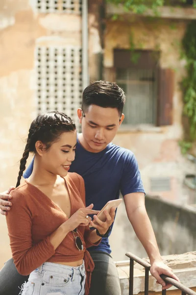 Young Asian couple standing together outdoors and using their mobile phone for online communication