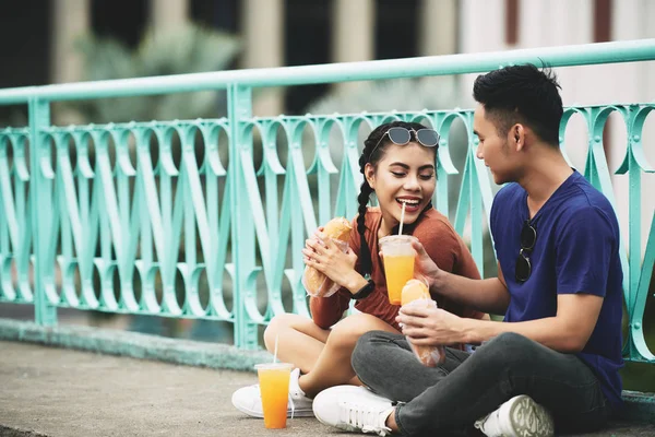 亚洲年轻夫妇坐在地上吃三明治和喝果汁在城市 — 图库照片