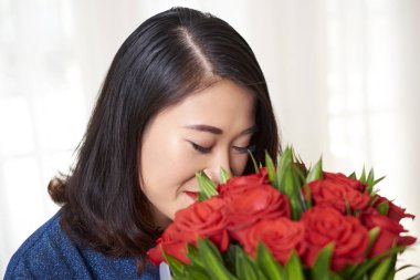 Genç Asyalı kadın kırmızı gül buketini kokluyor. Gözleri kapalı. Tatilde ona hediye veriyor.