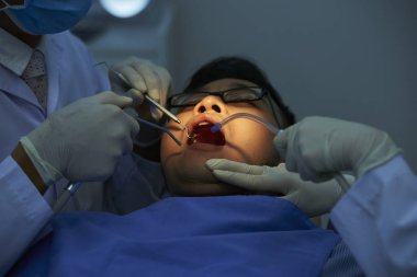 Diş hekimi ve asistanı diş kliniğinde dişlerini muayene ve tedavi ederken ağzını açan erkek hasta