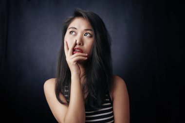 Genç ve güzel bir kız ayakta dikiliyor ve siyah arka plandan başka bir şeye bakıyor.