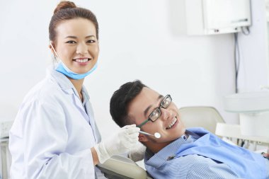 Kadın hemşirenin klinikte özel diş aletleri ile diş sandalyesinde genç bir erkeğe gülümseyen ve muayene eden portresi