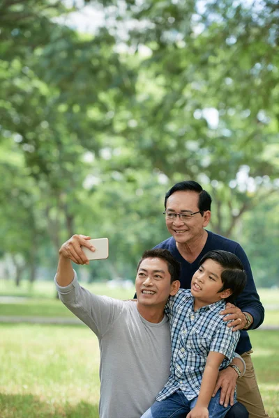 Grandfather, father and son photographing in park