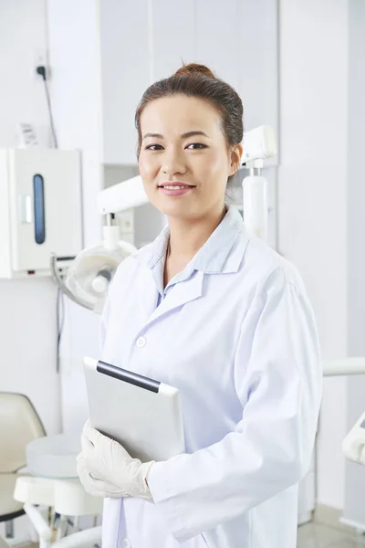 微笑的年轻牙医站在白色外套和持有数字平板电脑在诊所的肖像 — 图库照片