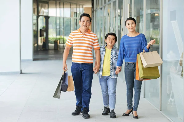 Alışveriş merkezinde yürüyen birçok kağıt torbaile Gülümseyen Vietnamlı aile