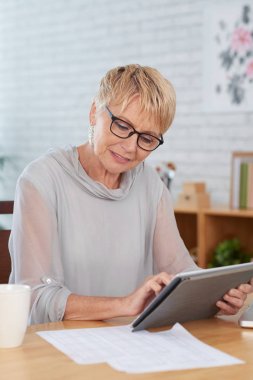 Olgun kadın evde dijital tablet üzerinde belgeleri okuma ve yazma masada oturan
