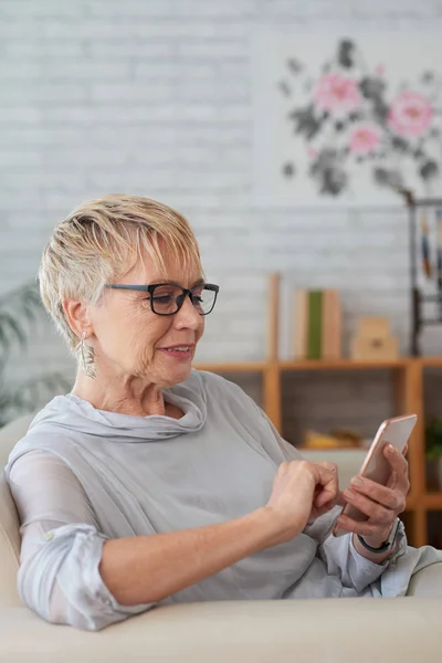 Ανώτερη Γυναίκα Γυαλιά Που Κάθονται Στον Καναπέ Πληκτρολογώντας Ένα Μήνυμα — Φωτογραφία Αρχείου
