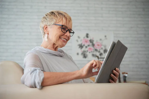 Uśmiechnięta Starsza Kobieta Siedzi Kanapie Komunikowanie Się Online Tablecie Cyfrowym — Zdjęcie stockowe