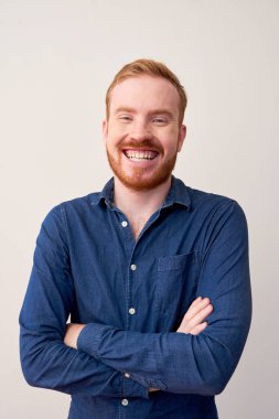 Genç mutlu kırmızı saçlı adam kot ceket gülerek ayakta ve beyaz arka plan üzerinde kamera bakarak portresi