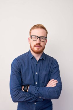 Kırmızı saçlı yakışıklı adam portresi gözlük ve kot ceket kolları ile ayakta ve beyaz arka planda kamera bakarak