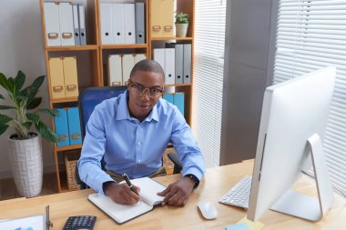 Siyah genç işadamı ofis masasında oturan ve not defterinde planları yazma