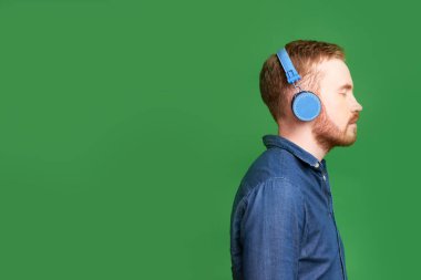 Kulaklıkla iyi müzik dinlerken gözlerini kapatan genç adam, yeşil ışıkta izole edilmiş.