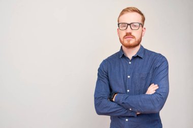 Kolları katlanmış ve kameraya bakan kızıl saçlı kendinden emin genç adamın portresi