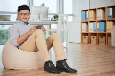 Yakışıklı Asyalı adam gülümseyerek ve akıllı telefon tutarken kameraya bakıyor 