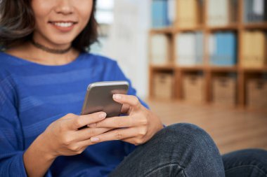 Ofiste dinlenirken gülümseyen ve akıllı telefonlara bakan kadın.