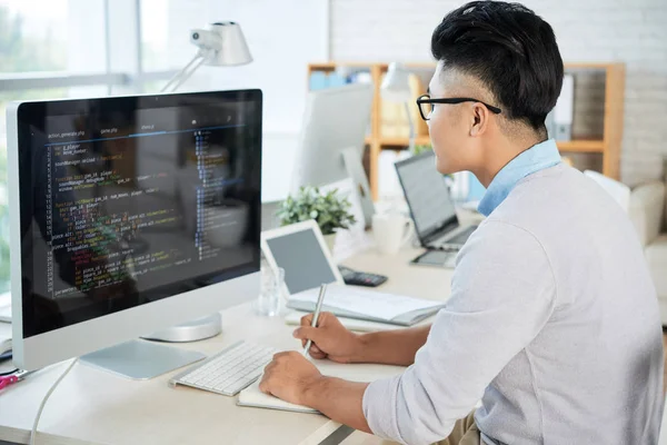 在现代办公室工作时 亚洲年轻人看电脑显示器和素描本的侧视图 — 图库照片