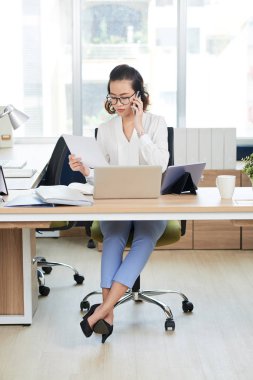 Telefon ederken iş belgesi okuyan genç bir kadın