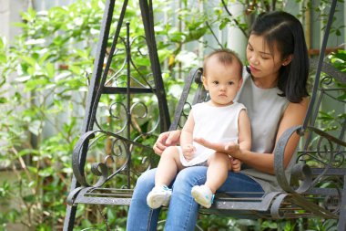 Genç Vietnamlı kadın kucağında küçük bir kızla salıncakta oturuyor.