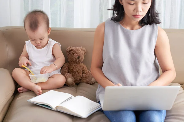 Piccolo Bambino Mangiare Quando Sua Madre Lavora Sul Computer Portatile — Foto Stock