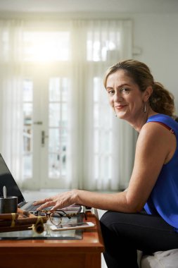 Olgun kadın masada oturan ve yazma ve evde dizüstü bilgisayar üzerinde çalışan portresi