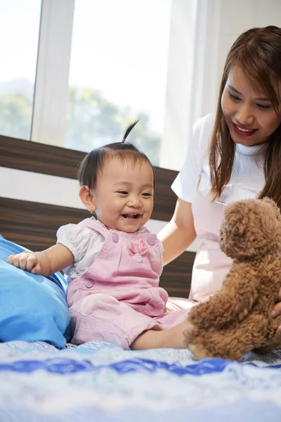 彼女の母親が与えているテディベアを見て幸せな小さなアジアの幼児の女の子 — ストック写真