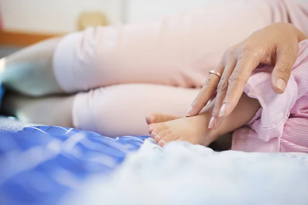 ベッドに横たわり 彼女を抱きしめると赤ちゃんの娘の足に触れる若い母親のトリミングされた受刑者 — ストック写真