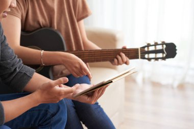 Kanepede birlikte oturan çift Kırpma yan görünümü, erkek elinde tablet ve bulanık arka plan üzerinde ekrana işaret akustik gitar ile kadın 