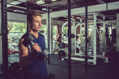 Ciddi genç adam pazı için dumbbells ile egzersizleri yapıyor