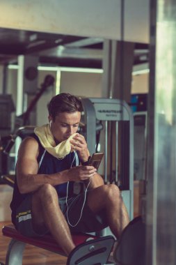 Fit genç adam havlu ile yüz silme ve setleri arasında telefon kontrol