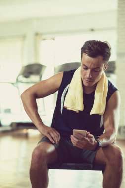 Terli fit adam spor salonunda bankta oturan ve onun akıllı telefon sosyal medya kontrol