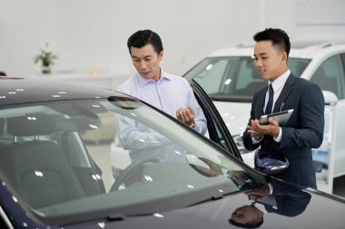 Yakışıklı genç araba bayilik işçi orta yaşlı müşteriye araba gösteren